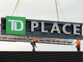 Workers lower the TD Place sign into place atop the massive scoreboard at TD Place stadium. Karen Martin says she was 'startled by the pure ugliness' of a similar green-and-white logo sign, which is mounted outside the stadium on the screen facing the Rideau Canal.