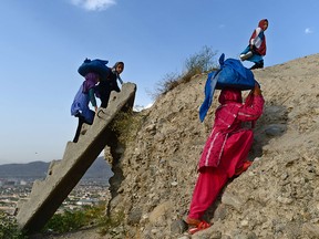 fghan children who work as street vendors climb a hilltop as they carry 'bolanis' (fried bread stuffed with potatoes) on their heads in Kabul on August 2, 2014.
