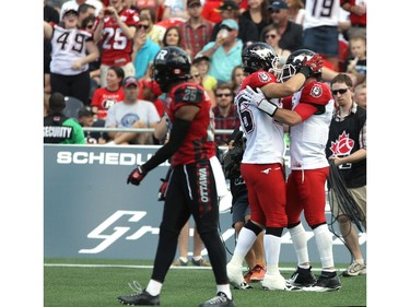 Brandyn Thompson #25 of the Ottawa Redblacks walks past as Rob Cote #26 (M) celebrates a touch down by Drew Tate #4 (R) of the Calgary Stampeders during a CFL match at TD Place in Ottawa on August 24, 2014.