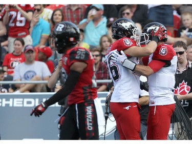 Brandyn Thompson #25 of the Ottawa Redblacks walks past as Rob Cote #26 (M) celebrates a touch down by Drew Tate #4 (R) of the Calgary Stampeders during a CFL match at TD Place in Ottawa on August 24, 2014.