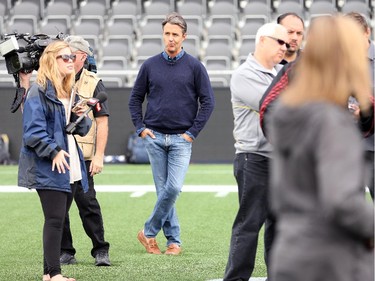 Former PM Brian Mulroney's son, Ben Mulroney, from E talk (centre), iwaits his turn to interview some players after practice.  Ottawa Redblacks run through a light practice Thursday, August 14, 2014 at TD Place stadium before Friday night's home game against the Edmonton Eskimos.