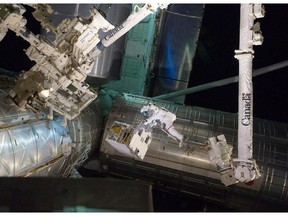 An astronaut rides on the International Space Station's robotic arm, emblazoned with the Canada logo.