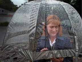 Jodie Chislett stays under her umbrella to read her iPad while waiting for a bus on Meadowlands Dr.
