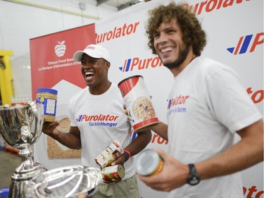 (L-R) The Ottawa  Redblacks QB, Henry Burris and Fury FC forward, Tom Heinemann smiles for the camera at the Ottawa Food Bank for Purolator Tackle Hunger weekend on Thursday, Aug. 14, 2014.  Fans attending the Redblacks and Fury FC games in Aug. 15 and 17 are encouraged to bring non-perishable food items or cash donations to the volunteers stationed at the stadium gates. Fans will have the opportunity to have a photo taken with the Grey Cup and North American Soccer League (NASL) Soccer Bowl trophy.