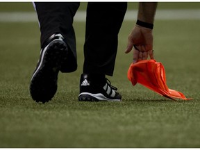 An official picks up a penalty flag off the turf as the B.C. Lions and Hamilton Tiger-Cats play during the second half of a CFL football game in Vancouver, B.C., on Friday August 8, 2014.