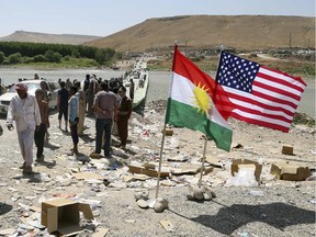 U.S. and Kurdish flags flutter in the wind while displaced Iraqis from the Yazidi community cross the Syria-Iraq border at Feeshkhabour bridge over the Tigris River at Feeshkhabour border point,  in northern Iraq, Sunday, Aug. 10, 2014. Kurdish authorities at the border believe some 45,000 Yazidis passed the river crossing in the past week and  thousands more are still stranded in the mountains.