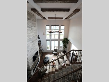 The two-storey family room soars 18 feet to an elaborate coffered ceiling intertwined with timber beams in one of several examples of the fusion of rustic, industrial and contemporary styles. The Restoration Hardware light fixture adds to the effect, along with the floor-to-ceiling fireplace surround in a tile with hints of stone and wood, and the sleek quartz mantel.