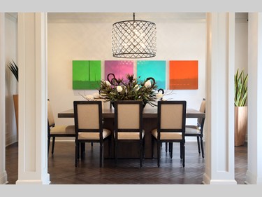 The dining room is a mirror of the living room, sitting opposite it and featuring the same chandelier, herringbone-patterned hardwood and lively art. Pillars offer an elegant entrance to the space.