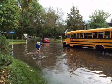 A school bus passes by a resident attempting to clear a storm drain at Edgeworth following a thunderstorm's passing on Friday, September 5, 2014.
