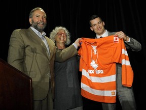 Edmonton Oilers hockey club captain Andrew Ference (right) is presented with an NDP hockey jersey from Canada's New Democratic Party (NDP) Leader Thomas Mulcair (left) and Alberta NDP MP Linda Duncan (middle) after Ference spoke at the NDP Caucus Strategy Session in Edmonton.