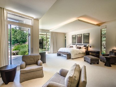 The master bedroom features an alcove with easy chairs and a view through the floor-to-ceiling windows of the backyard, including the pool and tennis court.