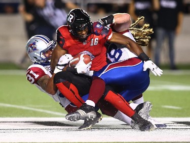 Marcus Henry #16 of the Ottawa Redblacks is tacked by Winston Venable #31 and Bear Woods #48 of the Montreal Alouettes after making a catch in the second quarter during a CFL game at TD Place Stadium on September 26, 2014.