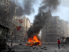 A Syrian youth walks near smoke and flames rising from a vehicle in a damaged street following a reported airstrike by government forces on April 4, 2014.