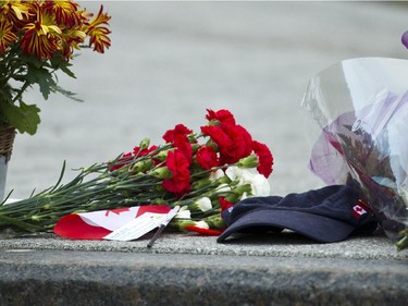 A memorial of flowers and a Canadian flag and a cap at the War Memorial. Police remain on the scene Oct 23