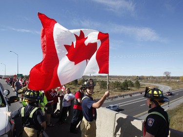 An Ottawa firefighter waves a Canadian Flag as crowds wait on an overpass at the Veterans Memorial Highway for a procession transporting the body of Cpl. Nathan Cirillo to pass by in Ottawa on Friday, October 24, 2014.