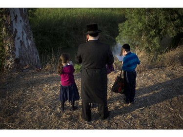 An ultra-Orthodox Jew and his children pray on the Hayarkon river bank as they participate in a Tashlich ceremony in the Israeli town of Ramat Gan near Tel Aviv, Israel, Thursday, Oct. 2, 2014. Tashlich, which means "to cast away" in Hebrew, is the practice by which Jews go to a large flowing body of water and symbolically "throw away" their sins by throwing a piece of bread, or similar food into the water before the Jewish holiday of Yom Kippur. The major Jewish holiday coincides with the Muslim holiday of Eid al-Adha, the first time this has happened since 1981.