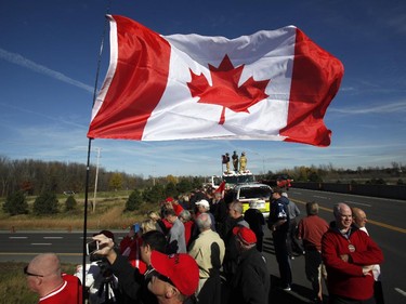 Crowds wave Canadian flags on an overpass at the Veterans Memorial Highway waiting for a procession transporting the body of Cpl. Nathan Cirillo to pass by in Ottawa on Friday, October 24, 2014.