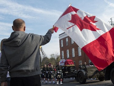 A man waves a Canadian flag while the casket makes its way through the streets of Hamilton