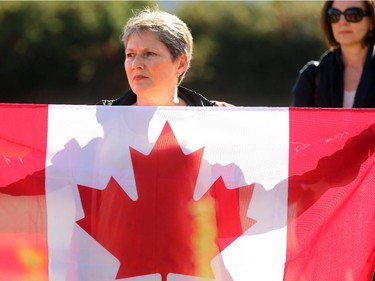 Janet Buske-Wichser holds a big Canadian flag in honour of the fallen soldier at the funeral home. The procession carrying the casket of  Cpl. Nathan Cirillo (recently gunned down in the terror attack at Ottawa's war memorial) leaves McEvoy-Shields funeral home in Ottawa Friday afternoon as it starts it's escorted procession home to Hamilton October 24, 2104.