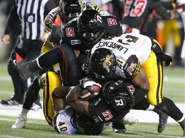 Jeremiah Johnson (27) of the Ottawa Redblacks is tackled by Simoni Lawrence and Eric Norwood (40) of the Hamilton Tiger-Cats during first half CFL action.