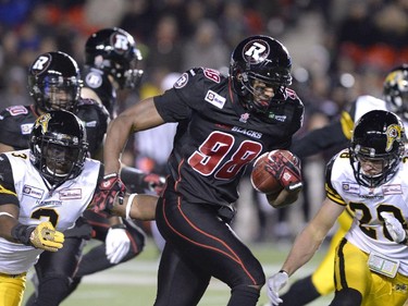 Ottawa Redblacks Marlon Smith (98) carries the ball against Hamilton Tiger-Cats Marc Beswick (3) and Emanuel Davis (20) during first half CFL action.