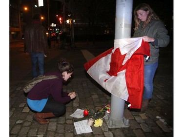 Mourners light a candle and tie a Canadian flag around a light pole near the National War Memorial after a soldier was killed near in Ottawa on Wednesday, October 22, 2014. A gunman turned the nation's capital into an armed camp Wednesday after he fatally shot an honour guard at "point blank" range at the National War Memorial before setting his sights on Parliament Hill.