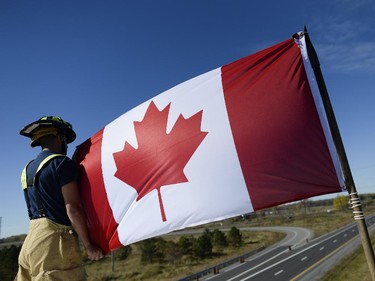 Ottawa Firefighter Jason Burchill holds up Canadian flag on top of a firetruck at Bankfield at the 416 to pay respects as the escort with the body of Nathan Cirillo is transported by hearse from Ottawa via Highway of Heroes to Hamilton on Friday, Oct. 24, 2014.
