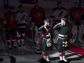 Ottawa Senators and New Jersey Devils players stand shoulder to shoulder around members of the Argyle and Sutherland Highlanders during the playing of O Canada before the NHL game in Ottawa Saturday October 25, 2014.