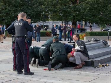 Police, bystanders and soldiers aid a fallen soldier at the War Memorial as police respond to an apparent terrorist attack in Ottawa.