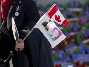 A woman holds a Canadian flag and the images of Cpl. Nathan Cirillo and Warrant Officer Patrice Vincent, the two fallen Canadian Forces members, as she stands near the National War Memorial after the Remembrance Day ceremony in Ottawa on Tuesday, Nov. 11, 2014.