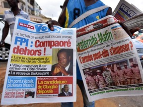 A street vendor holds two newspapers bearing headlines on the situation in Burkina Faso and reading (at left) ''Compaore out!" and (at right) ''After the resignation of Compaore, Can the army impose itself?" on November 3, 2014 in Abidjan.  Burkina Faso's military vowed to install a unity government after tightening its control over the west African nation, firing tear gas and shots in the air to disperse protesters denouncing an army power grab.