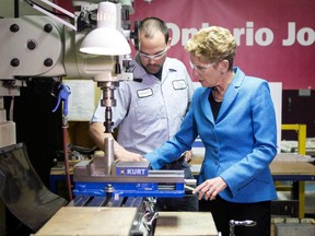 Ontario Premier and Liberal Leader Kathleen Wynne, right, is shown how to use a piece of machinery by employee Christopher Rembacz, as she tours Cyclone MFG Inc., a company which manufactures parts for the aviation industry, during a campaign stop in Mississauga, Ont., on Tuesday, May 13, 2014.