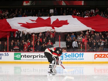 A large Canadian flag passes through the stands as Robin Lehner #40 of the Ottawa Senators focuses during the singing of the national anthems.