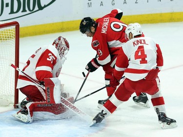 Detroit Red Wings goaltender Jimmy Howard (35) watches the puck as teammate Jakub Kindl (4) and Ottawa Senators' Milan Michalek (9) battle in front of the net during first period NHL hockey action.