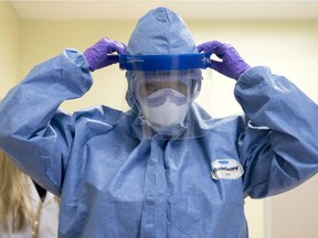 Infection Prevention and Control professional Nimo Mohamoud puts on a face shield, comprising part of the Personal Protective Equipment (PPE) designed for health-care providers working with patients with the Ebola virus during a training simulation in Ottawa on Friday, Oct. 31, 2014.