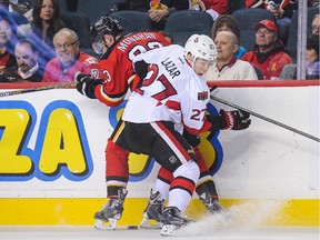 Sean Monahan #23 of the Calgary Flames is checked by Curtis Lazar #27 of the Ottawa Senators during an NHL game at Scotiabank Saddledome on November 15, 2014 in Calgary, Alberta, Canada.