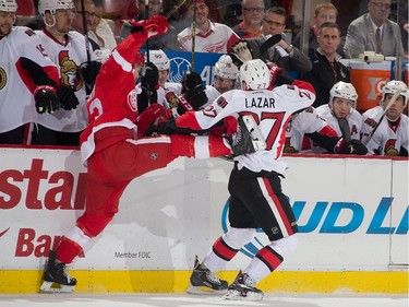 Curtis Lazar #27 of the Ottawa Senators body checks Darren Helm #43 of the Detroit Red Wings in front of the bench.