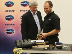 Prime Minister Stephen Harper and employee Andrew Earle look over devices fabricated on 3-D printers at The National Research Council building in London, Ont.
