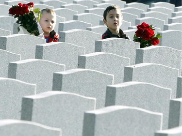 Three-year-old Soren Mason and his six-year-old brother Ronin carry flowers through the National Military Cemetery to place on their uncle's, Capt. Linden Mason's headstone while they take part in Remembrance Day ceremonies in Ottawa, Tuesday November 11, 2014 .