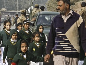 A plainclothes security officer escorts students evacuated from a school as Taliban fighters attack another school nearby, killing more than 100 people, mostly children, in Peshawar, Pakistan, Tuesday, Dec. 16, 2014.
