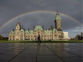A woman walks on Parliament Hill as a rainbow arches over the East Block on Tuesday, Oct. 7, 2014.