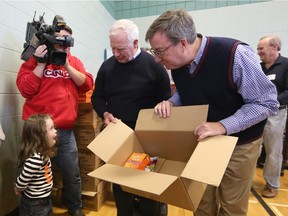 His Excellency the Right Honourable David Johnston, Governor General of Canada, centre, and Jim Watson, Mayor of Ottawa, right, get a package of stuffing from Isla Learmonth, 4, left,to pack in a hamper to deliver to families in need in conjunction with the Caring and Sharing Exchange on December 19.