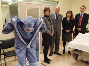 Judith Bosse (left to right), Assistant Deputy Minister at the Public Health Agency of Canada, Defence Minister Rob Nicholson, Health Minister Rona Ambrose and Dr. Gregory Taylor, Canada's Chief Public Health Officer, watch as nurse Adina Popalyar demonstrates how to remove protective clothing after treating a hypothetical Ebola patient.