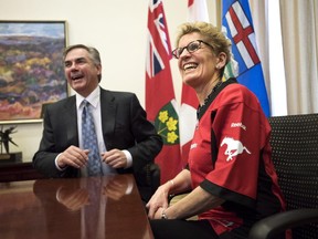 Ontario Premier Kathleen Wynne, right, wears a Calgary Stampeders jersey while meeting with Alberta Premier Jim Prentice following a friendly bet on the Grey Cup at Queen's Park Wednesday.