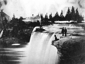 Man in top hat sitting on ledge above Rideau Falls, date unknown.
