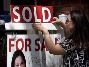 A real estate agent puts up a 'sold' sign in front of a house in Toronto.