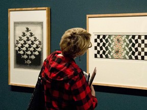 A reporter looks at a piece of work from artist M.C. Escher on display at the National Gallery of Canada in Ottawa on Thursday, Dec. 18, 2014., during a media preview of 'M.C. Escher: the Mathemagician.' The show is on view from Dec 20, 2014 till May 3, 2015. The pieces pictured are 'Sky and Water I' at left and 'Metamorphosis (Bees)' right.