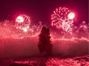 A wave crashes on two girls hugging as they usher in the new year, while fireworks explode over Copacabana beach, during New Year celebrations in Rio de Janeiro, Brazil, Thursday, Jan. 1, 2015.