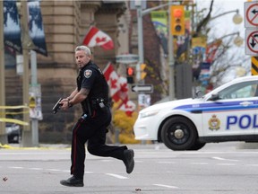 An Ottawa police officer runs with his weapon drawn in Ottawa on Wednesday Oct.22, 2014.Police are expanding a security perimeter in the heart of the national capital after a gunman opened fire and wounded a soldier at the National War Memorial before injuring a security guard on Parliament Hill, where he was reportedly shot dead by Parliament's sergeant-at-arms.