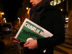 A journalist holds an early copy of a Charlie Hebdo magazine while delivering a news report outside the offices of Liberation Newspaper Group on January 13, 2015 in Paris, France.